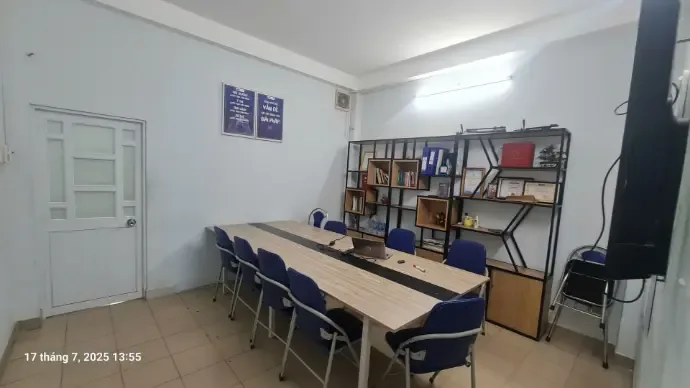 Phòng họp có bàn dài, ghế xanh và kệ sách
